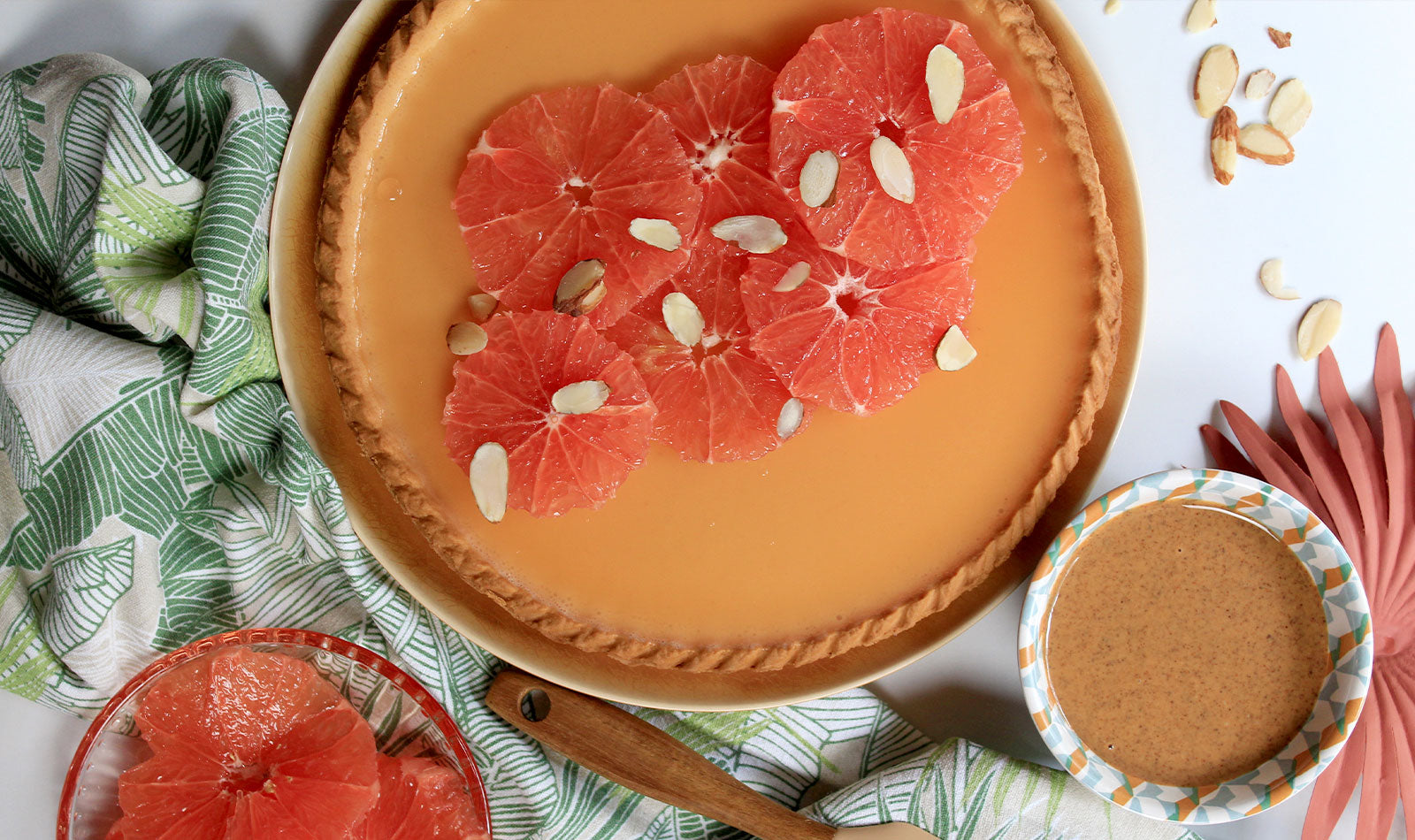 A large tart with a peach colored gelee and slices of pink grapefruit with sliced almonds as a garnish.
