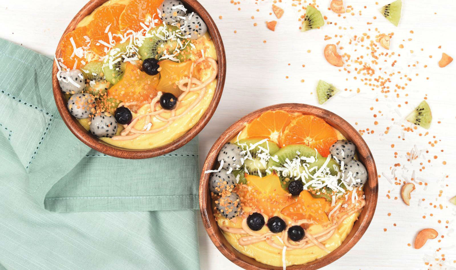 Wooden bowls filled to the brim with Mango Cashew smoothie and topped with fresh dragon fruit, star fruit, berries and more. 