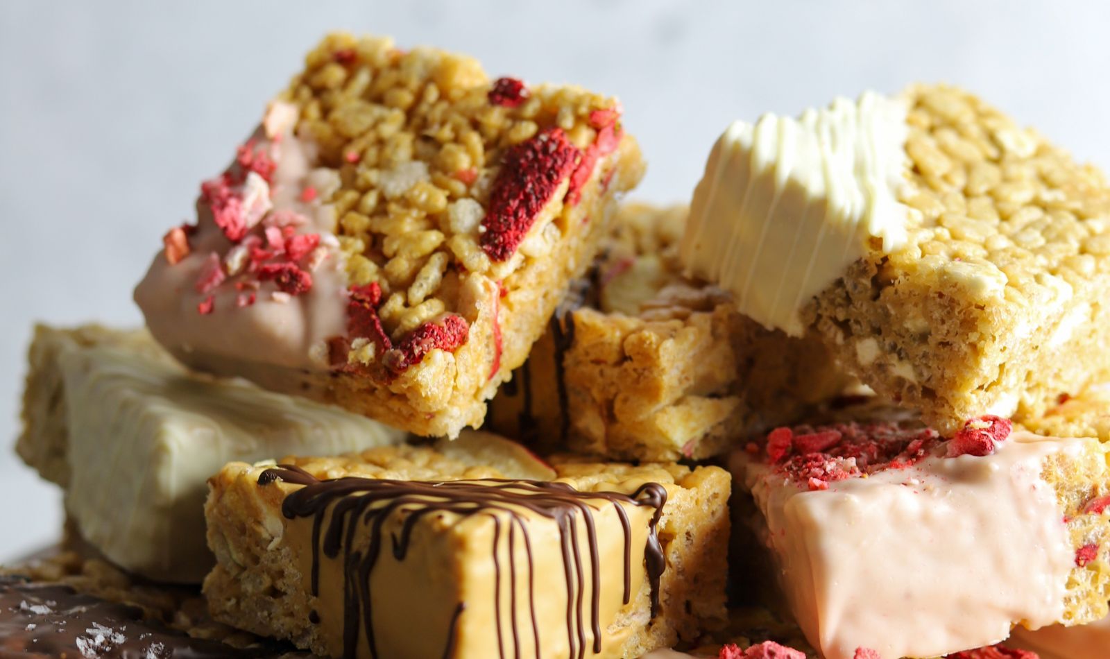 Marshmallow nut butter squares topped with melted chocolate and freeze-dried fruit, stacked into a pile.