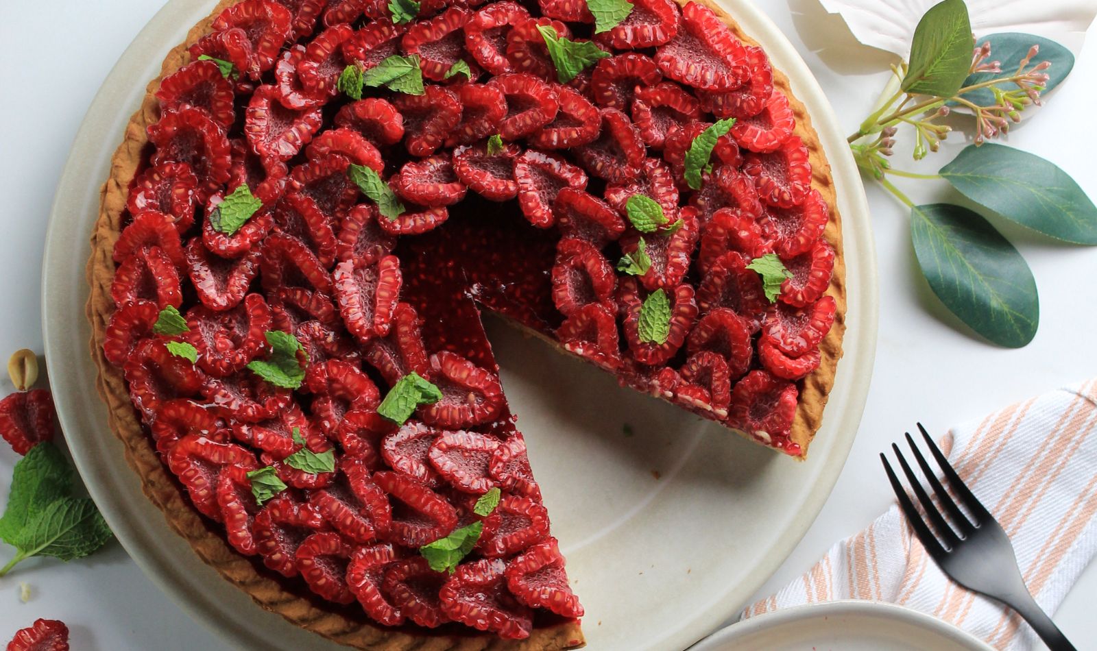 Peanut Butter Raspberry Tart with half cut raspberries arranged in rings around the edge of the tart flacked with fresh mint.