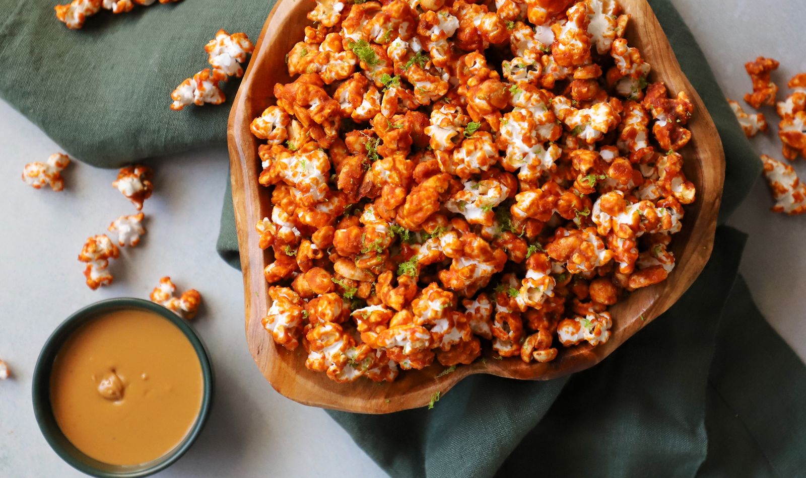 Sweet and spicy red curry peanut popcorn coated in a vibrant red-orange caramel, garnished with fresh lime zest, and served in an wooden bowl
