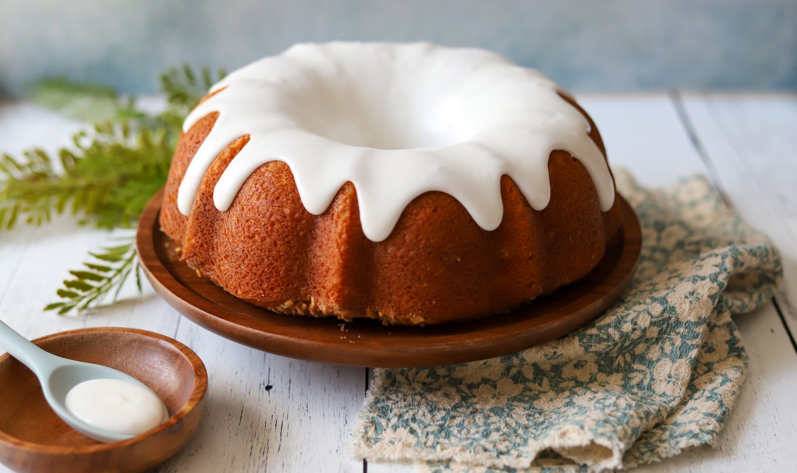 Coffee cake bundt with almond butter streusel, golden brown with a drippy white glaze, served on a rustic table with a cozy cottage-style background
