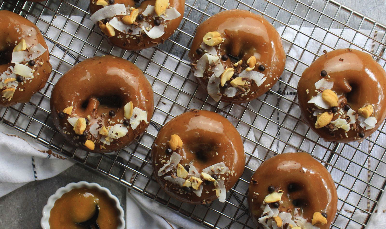 Glistening chocolate-glazed donuts with toppings on a metal cooling rack.